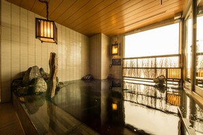 A traditional Japanese onsen with a wooden interior, a stone bath, and a view of trees through a window. - Dormy Inn Express Kakegawa Natural Hot Spring (Kakegawa)