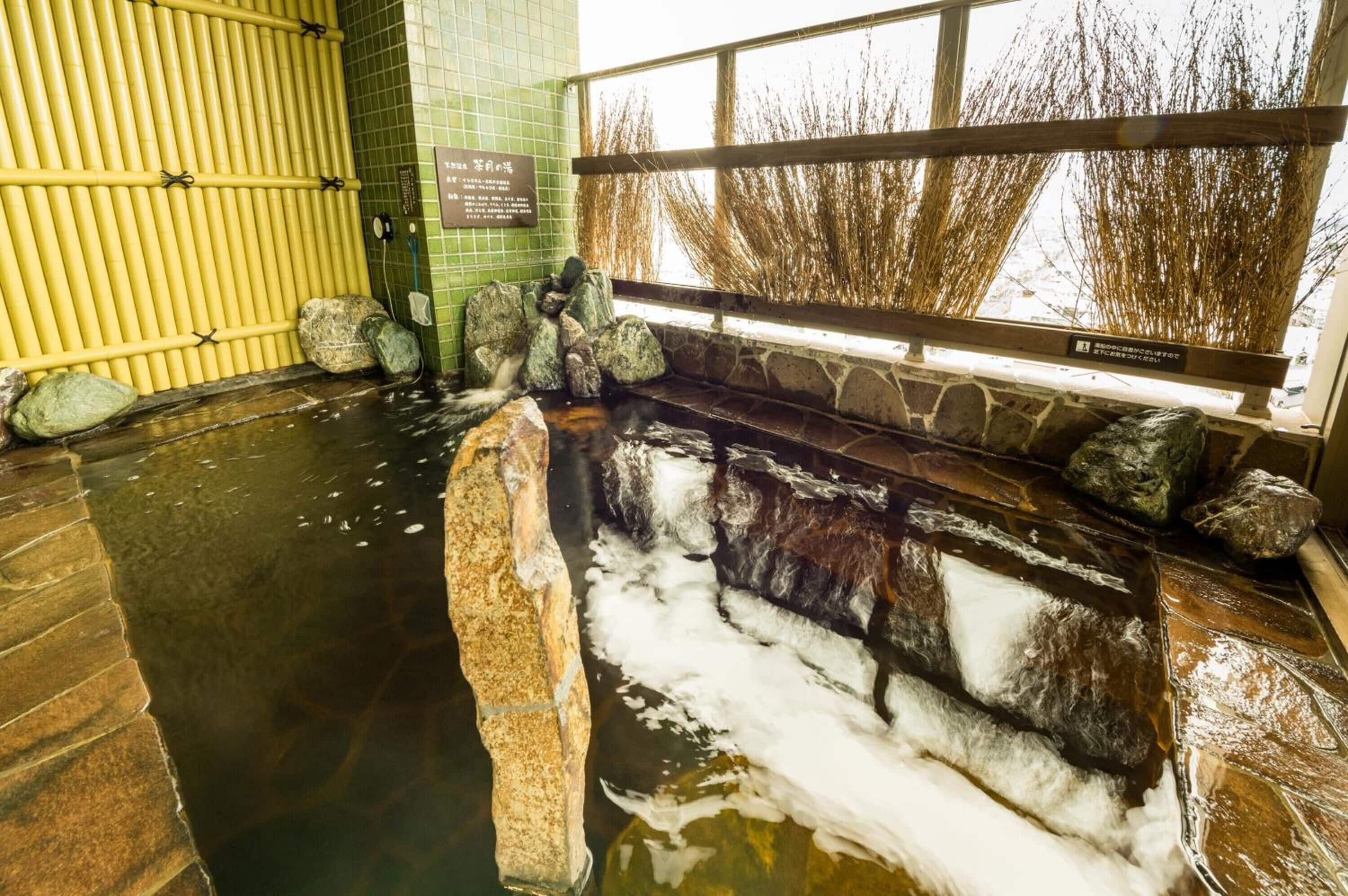 Un área de aguas termales con un banco de piedra, rocas y una barandilla de madera.