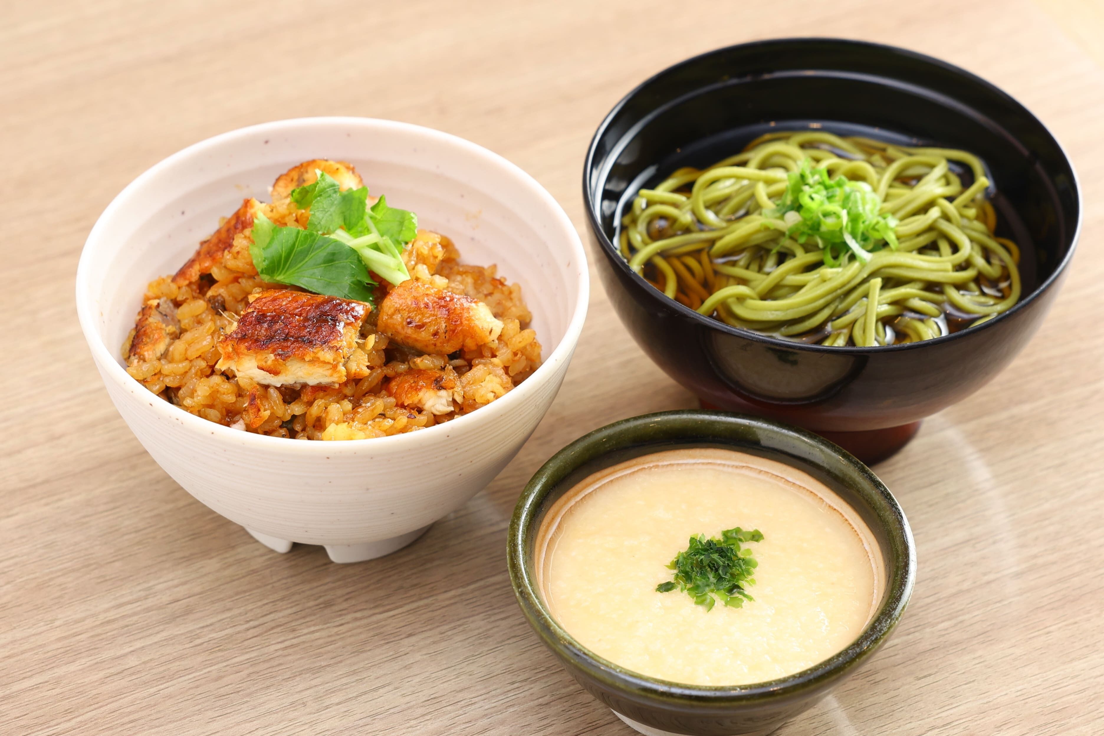 A bowl of food with a green garnish, a bowl of noodles, and a small bowl of soup.