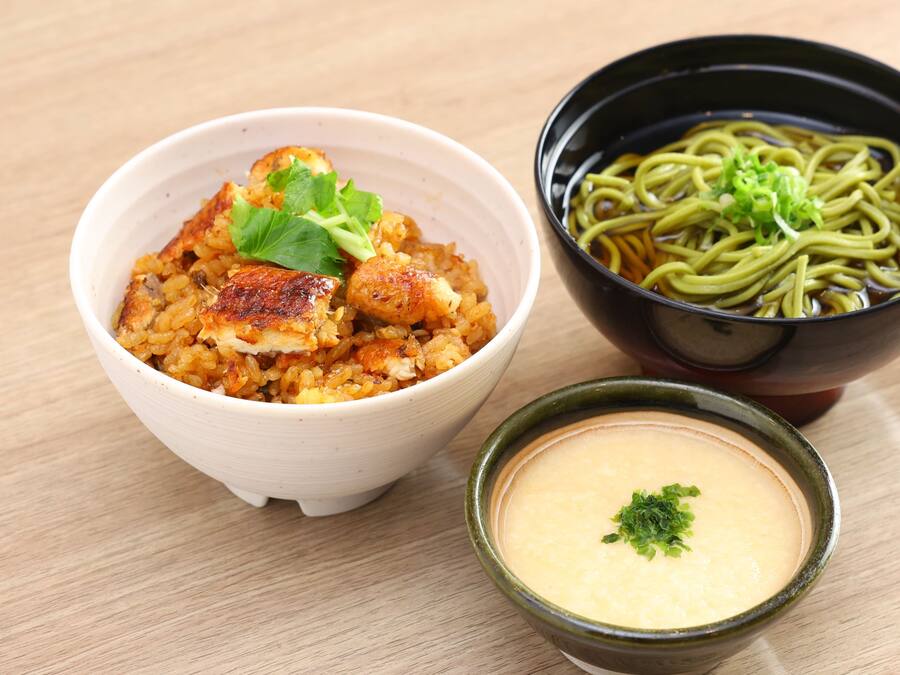 A bowl of food with a green garnish, a bowl of noodles, and a small bowl of soup.
