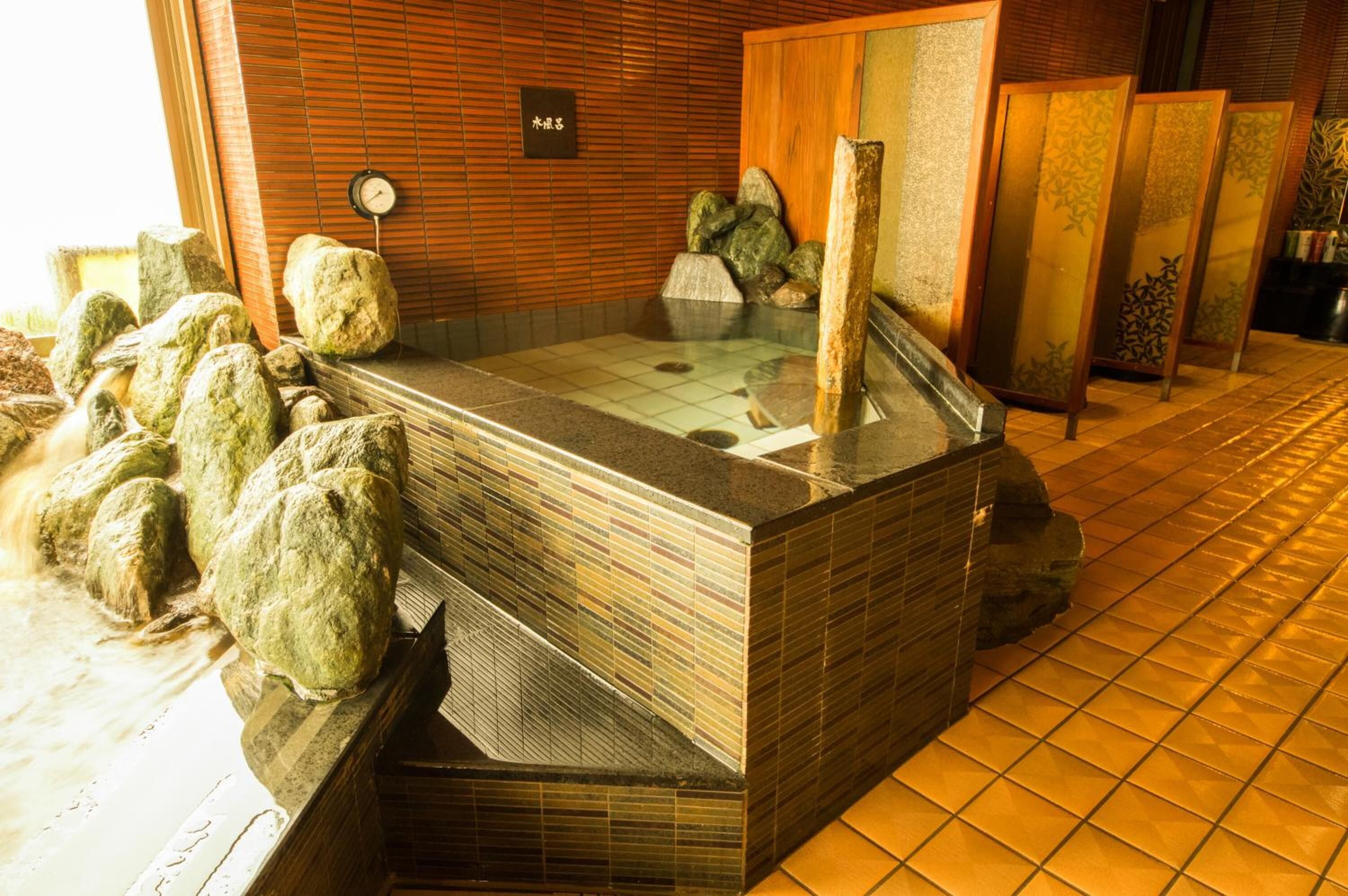 Un área de baño termal con suelo de baldosas, bancos de madera y pared de piedra.