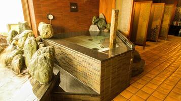 Un área de baño termal con suelo de baldosas, bancos de madera y pared de piedra.