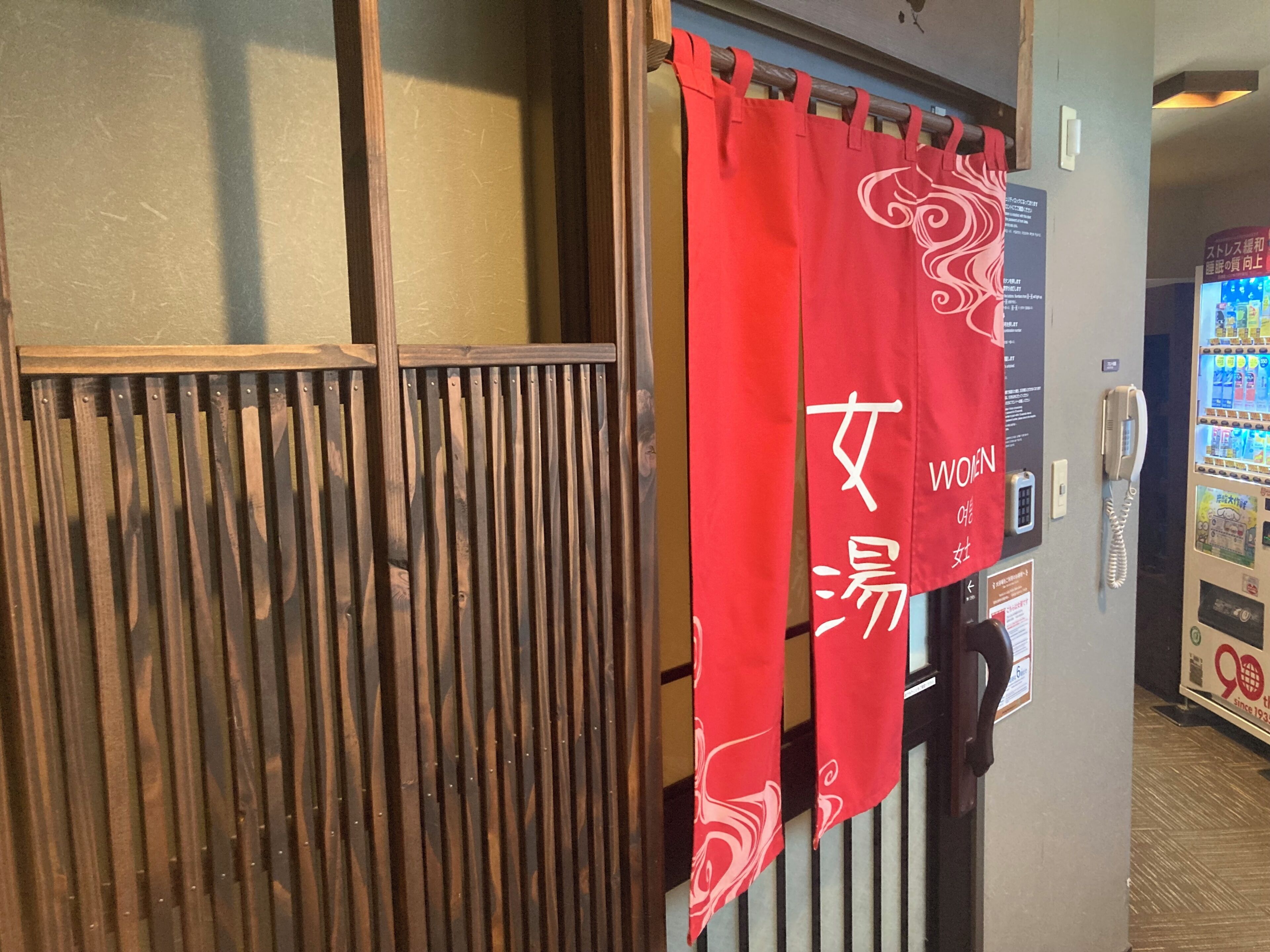 A wooden partition with vertical slats, a red curtain with white text, and a vending machine with various items.