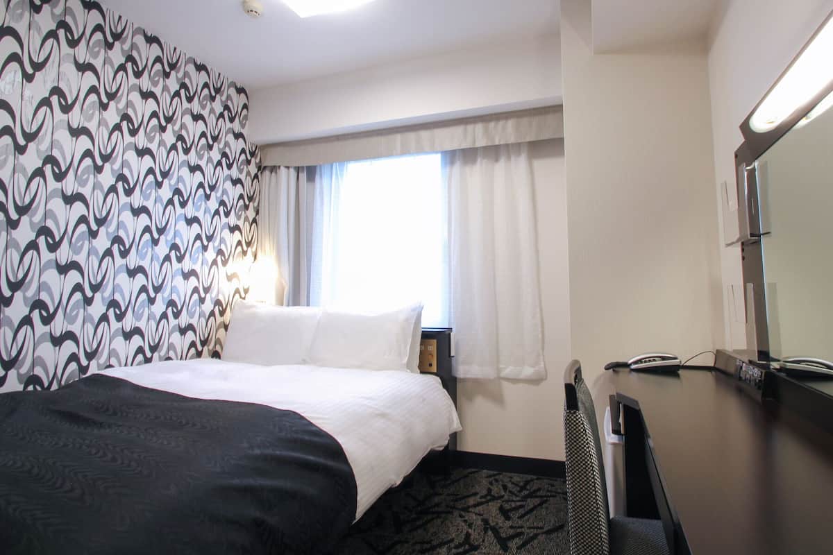 Een hotelkamer met een bed, een bureau met telefoon en een raam met gordijnen.