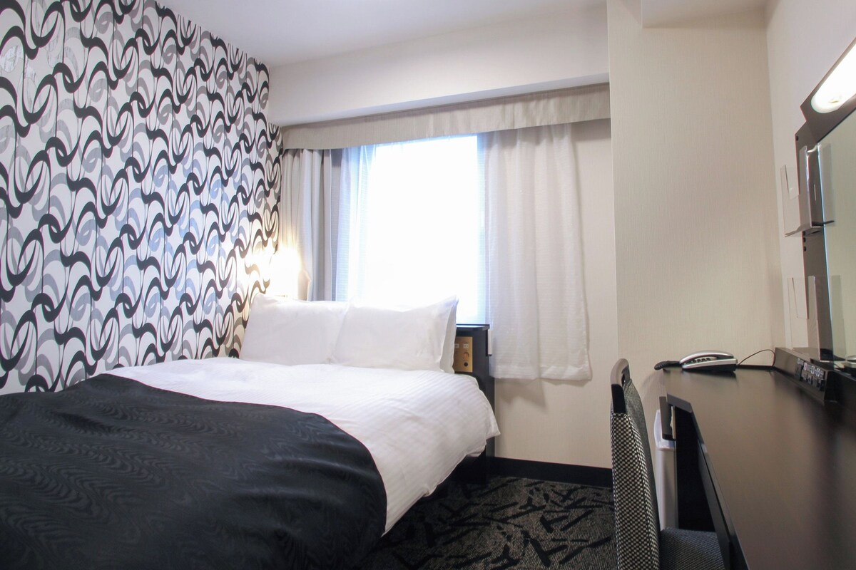 Une chambre d’hôtel avec un lit, un bureau, un téléphone et une fenêtre avec des rideaux.