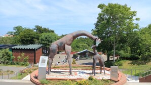 Een dinosaurusbeeld in een aangelegde tuin met een gebouw op de achtergrond.