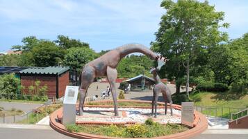 Una estatua de dinosaurio en un área ajardinada, con un edificio al fondo.