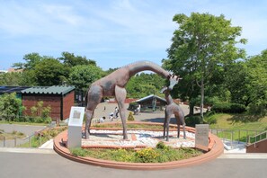 Une statue de dinosaure dans un espace aménagé, avec un bâtiment en arrière-plan.