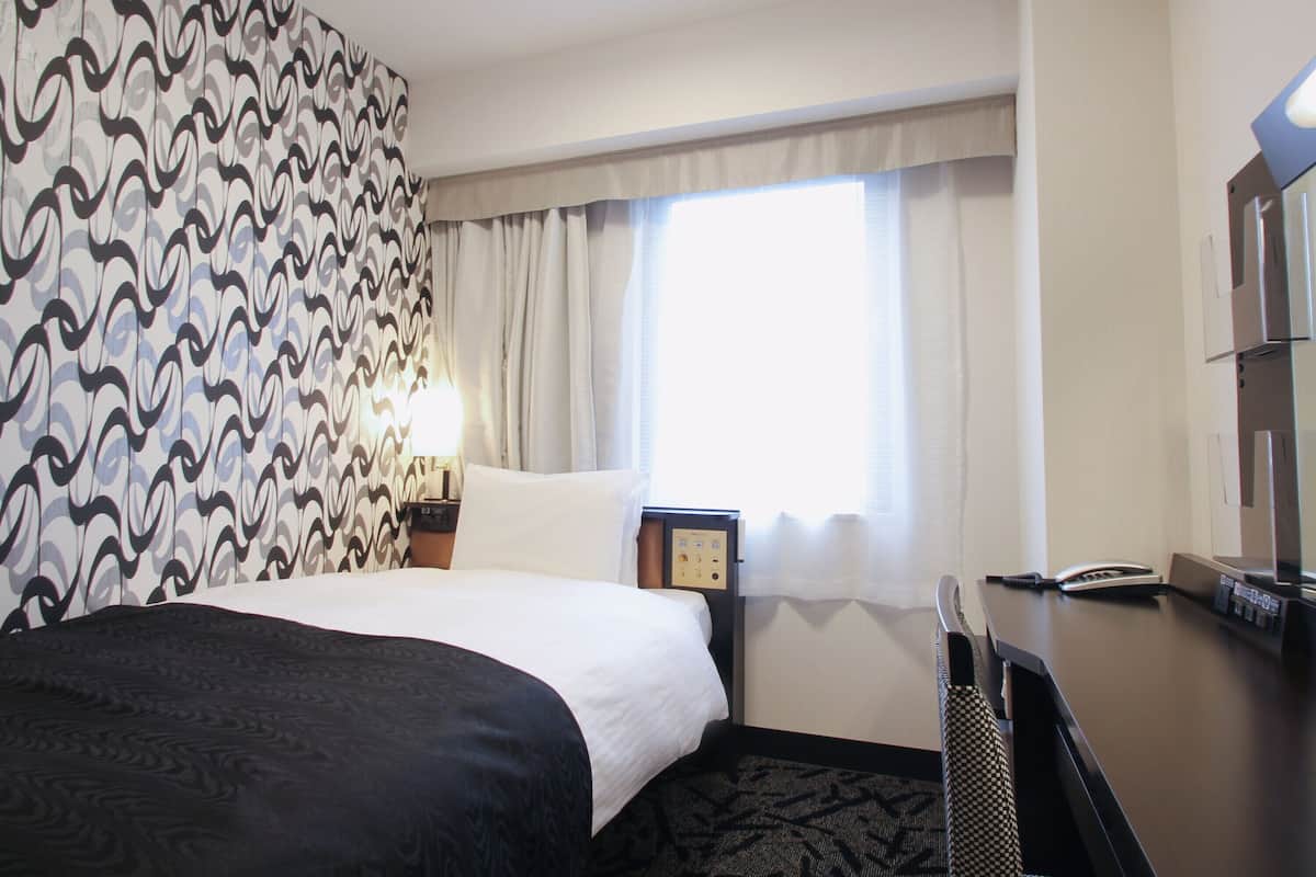 Een hotelkamer met een bed, een bureau, een telefoon en een raam met gordijnen.