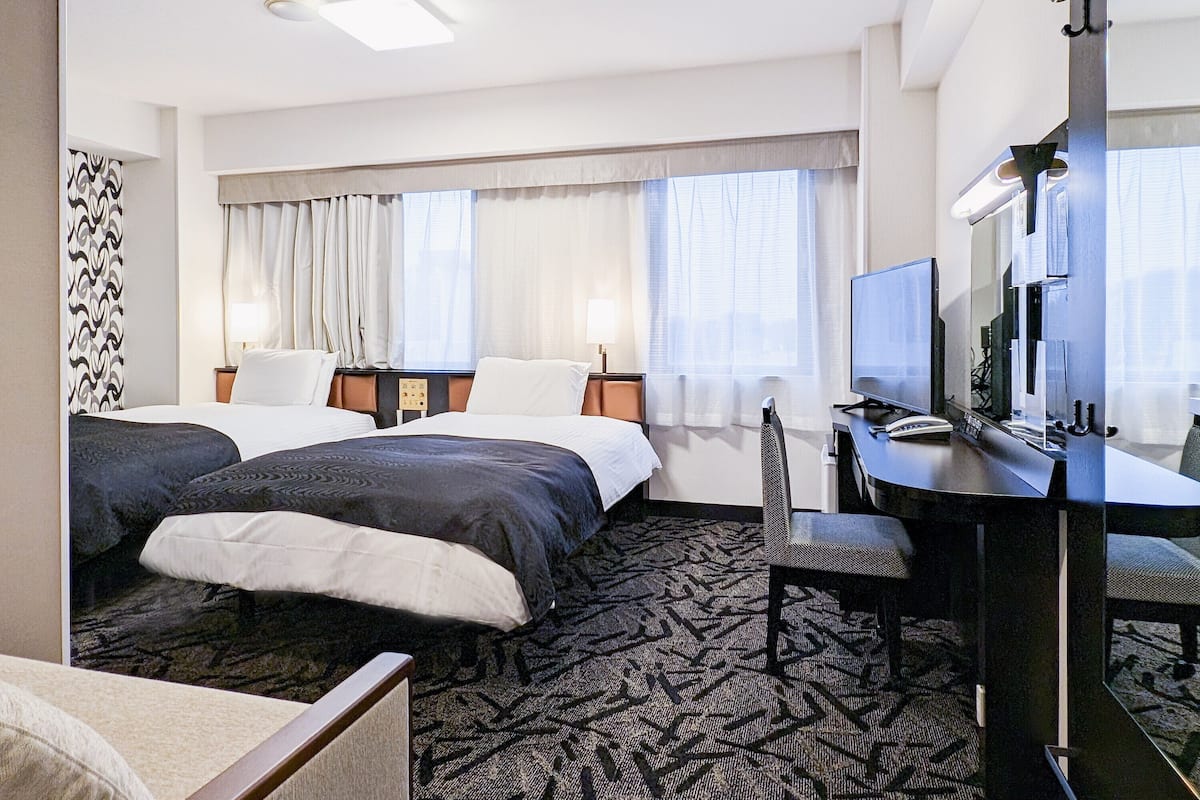 Een hotelkamer met twee bedden, een bureau met een computer, een stoel en een televisie.