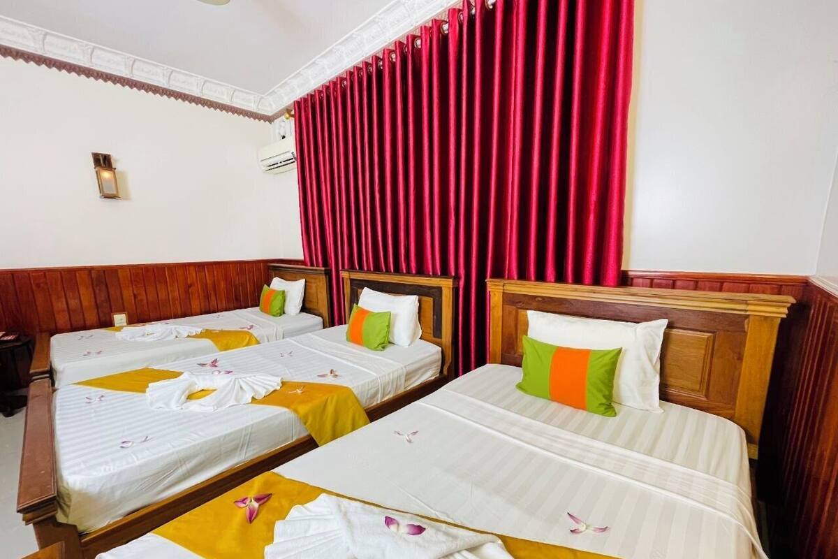 Een hotelkamer met drie bedden, elk voorzien van een witte spreidek en kussens, en een houten hoofdbord.