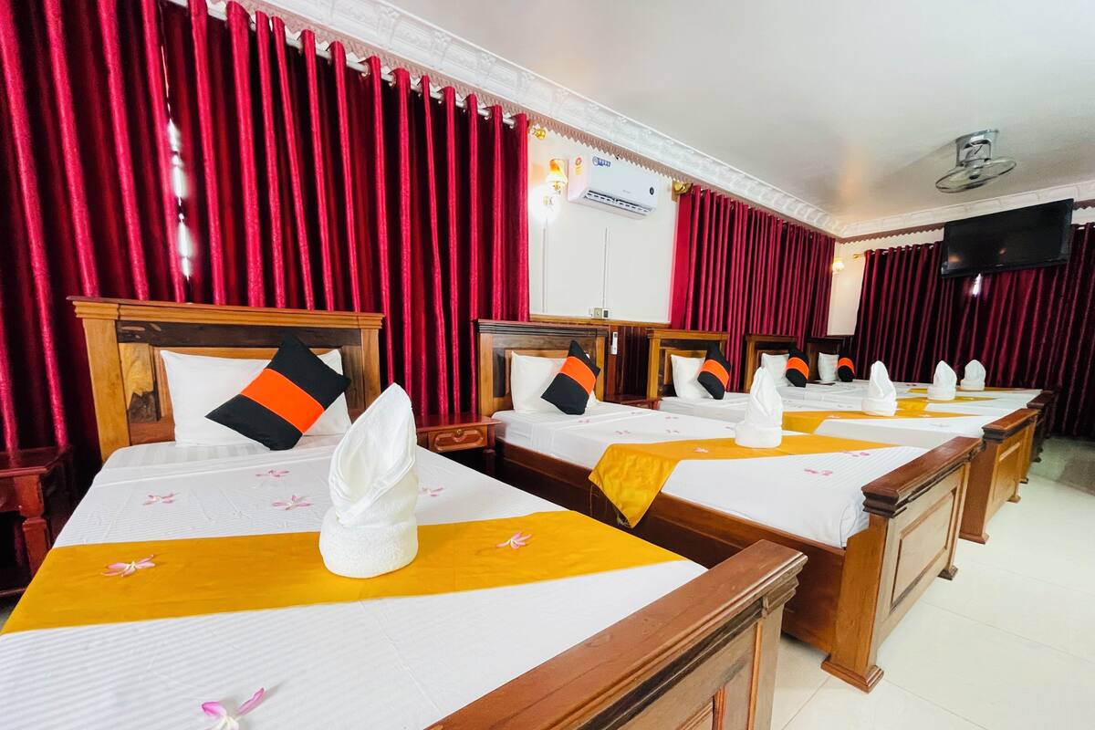 Een hotelkamer met meerdere bedden, elk voorzien van een witte sprei, oranje lopers en witte handdoeken.