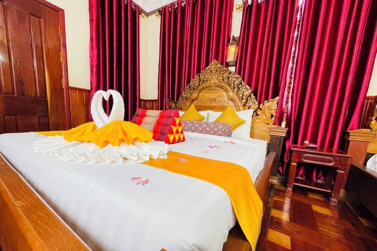 Een hotelkamer met een houten bed, rode gordijnen en een decoratief hoofdeinde.