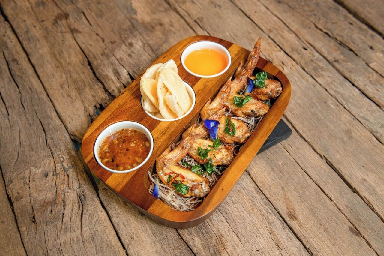 Un plateau de service en bois avec du poisson grillé, deux sauces pour tremper et une portion de pain plat.
