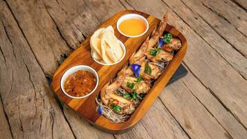 Un plateau de service en bois avec du poisson grillé, deux sauces pour tremper et une portion de pain plat.