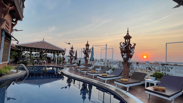 A rooftop pool with lounge chairs, a decorative statue, and a sunset view. - Okay 1 Villa (Siem Reap)