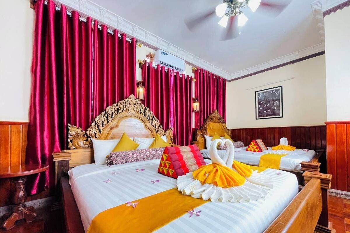 Een hotelkamer met twee bedden, rode gordijnen, een decoratief hoofdbord en een afbeelding in een lijst aan de muur.