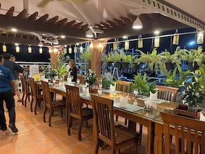 A restaurant with wooden tables and chairs, potted plants, and hanging lights. - Okay 1 Villa (Siem Reap)