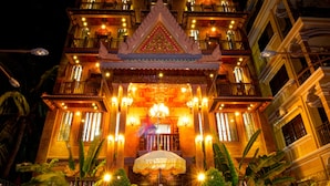 A multi-story building with balconies, a central entrance with a decorative canopy, and potted plants in the foreground. - Okay 1 Villa (Siem Reap)