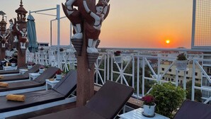 A rooftop terrace with lounge chairs, a decorative tree, and a sunset view. - Okay 1 Villa (Siem Reap)