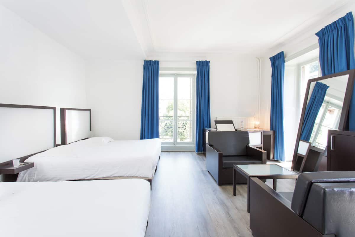 Une chambre d’hôtel avec deux lits, un bureau, une chaise et un grand miroir.