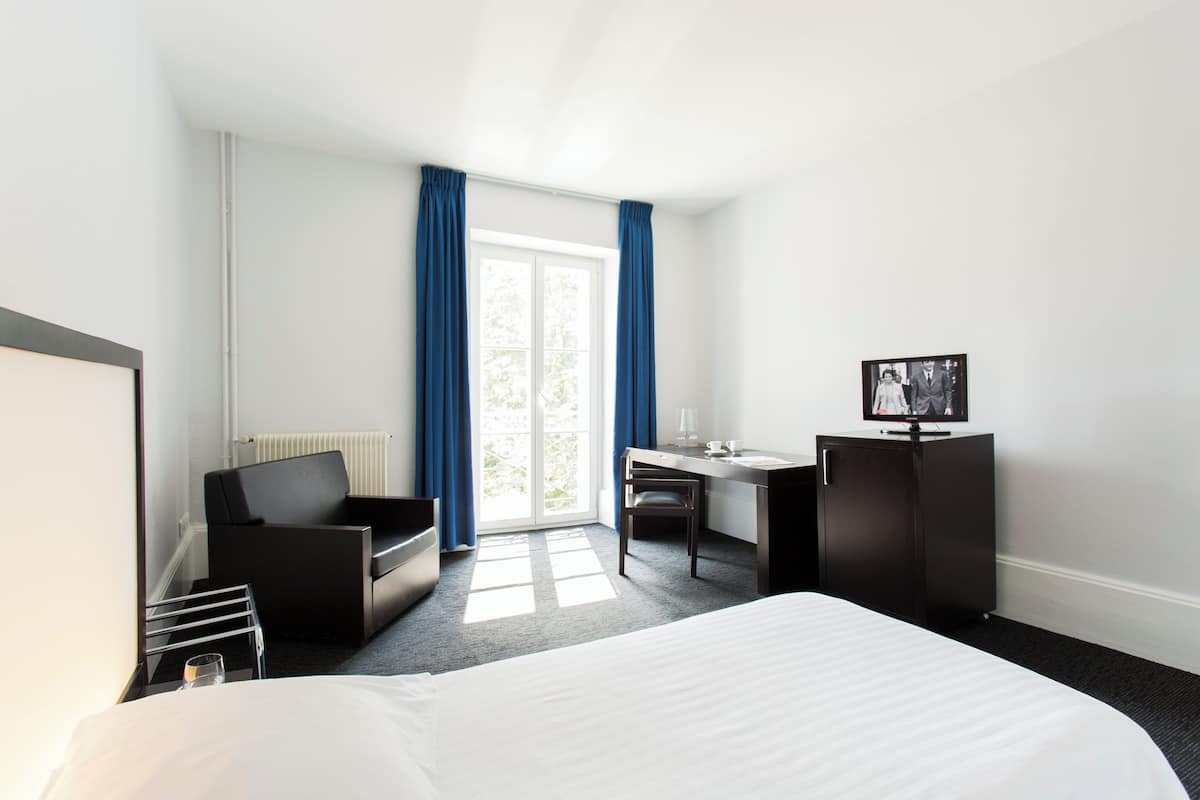 Une chambre d’hôtel équipée d’un lit, d’un bureau, d’une chaise, d’une télévision et d’une fenêtre avec des rideaux.