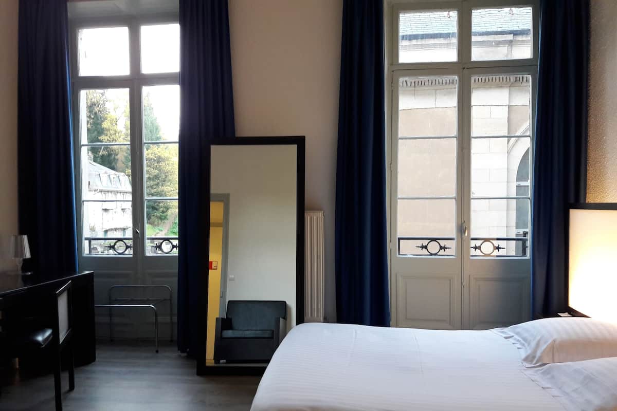 Une chambre d’hôtel équipée d’un lit, d’un bureau, d’une chaise, d’un grand miroir et d’une fenêtre avec des rideaux.