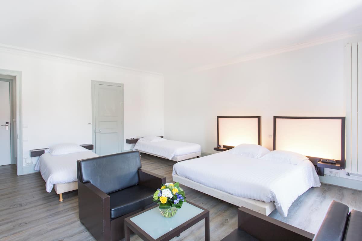 Une chambre d’hôtel avec deux lits simples, un canapé, une petite table sur laquelle est posé un vase de fleurs, et des lampes de chevet.