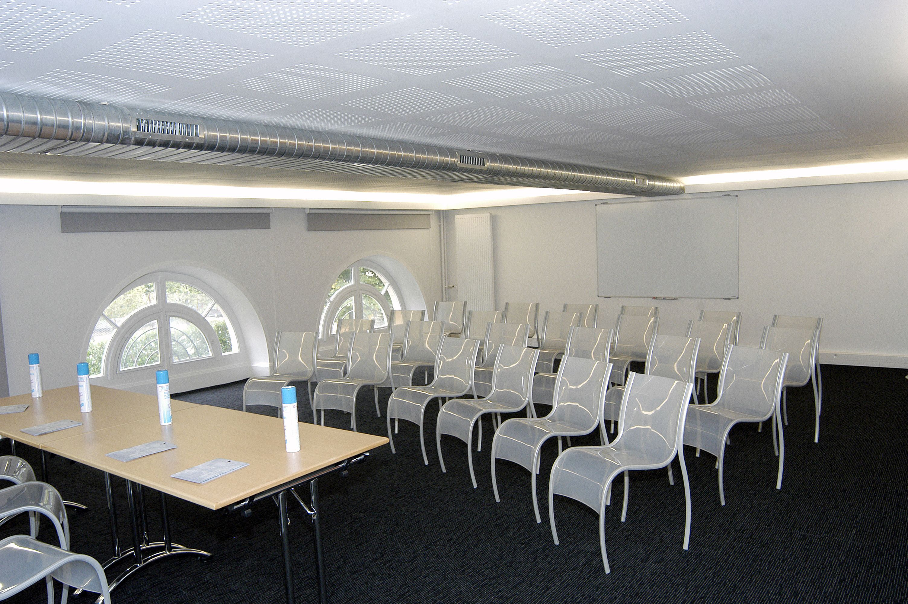 Une salle de conférence avec une longue table, des chaises, un écran de projection et des fenêtres.