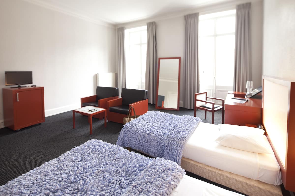 Une chambre d’hôtel avec deux lits, un bureau, une chaise, une télévision et une armoire.