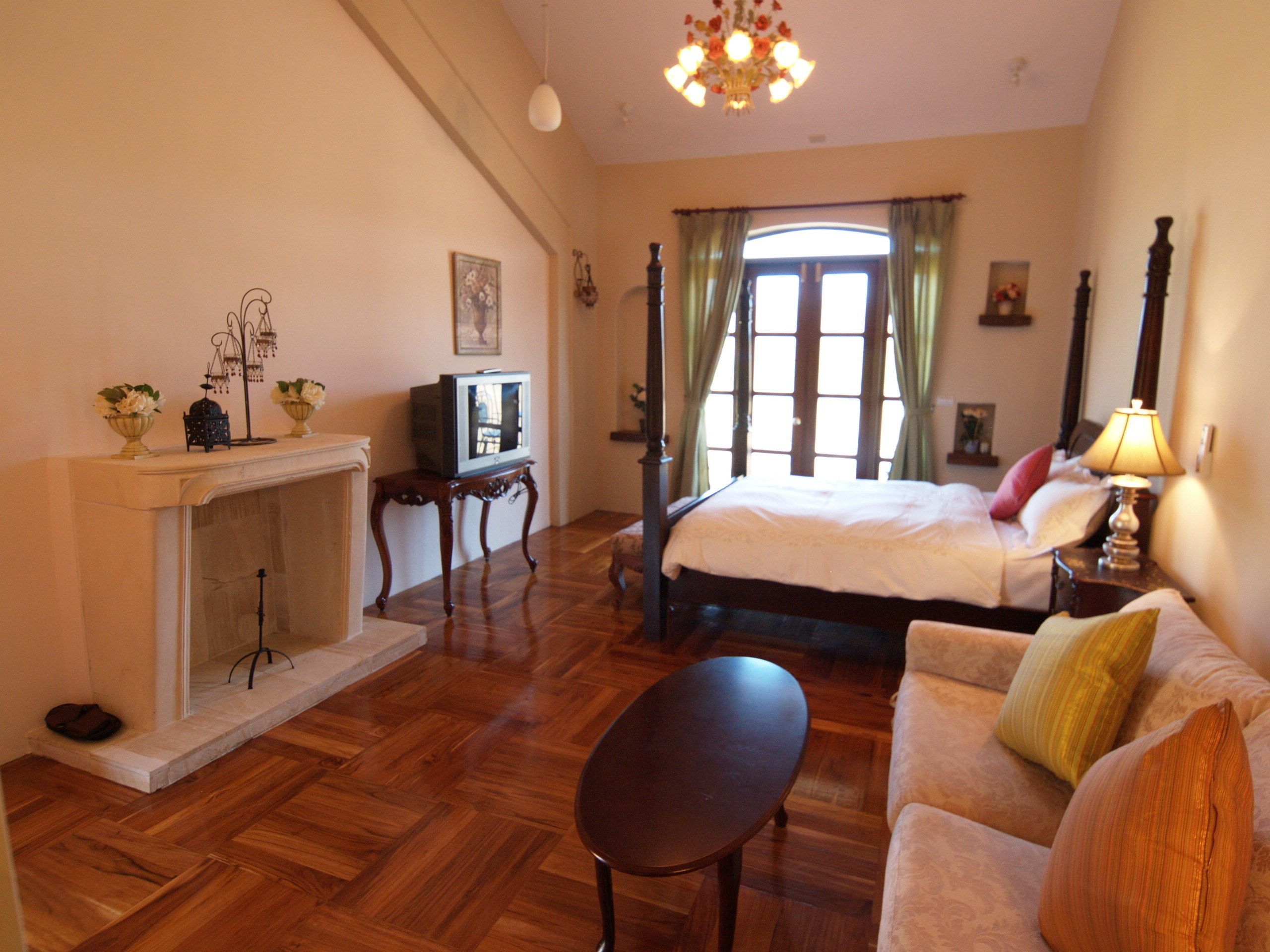 A room with a bed, a sofa, a small table, a fireplace, and a television.