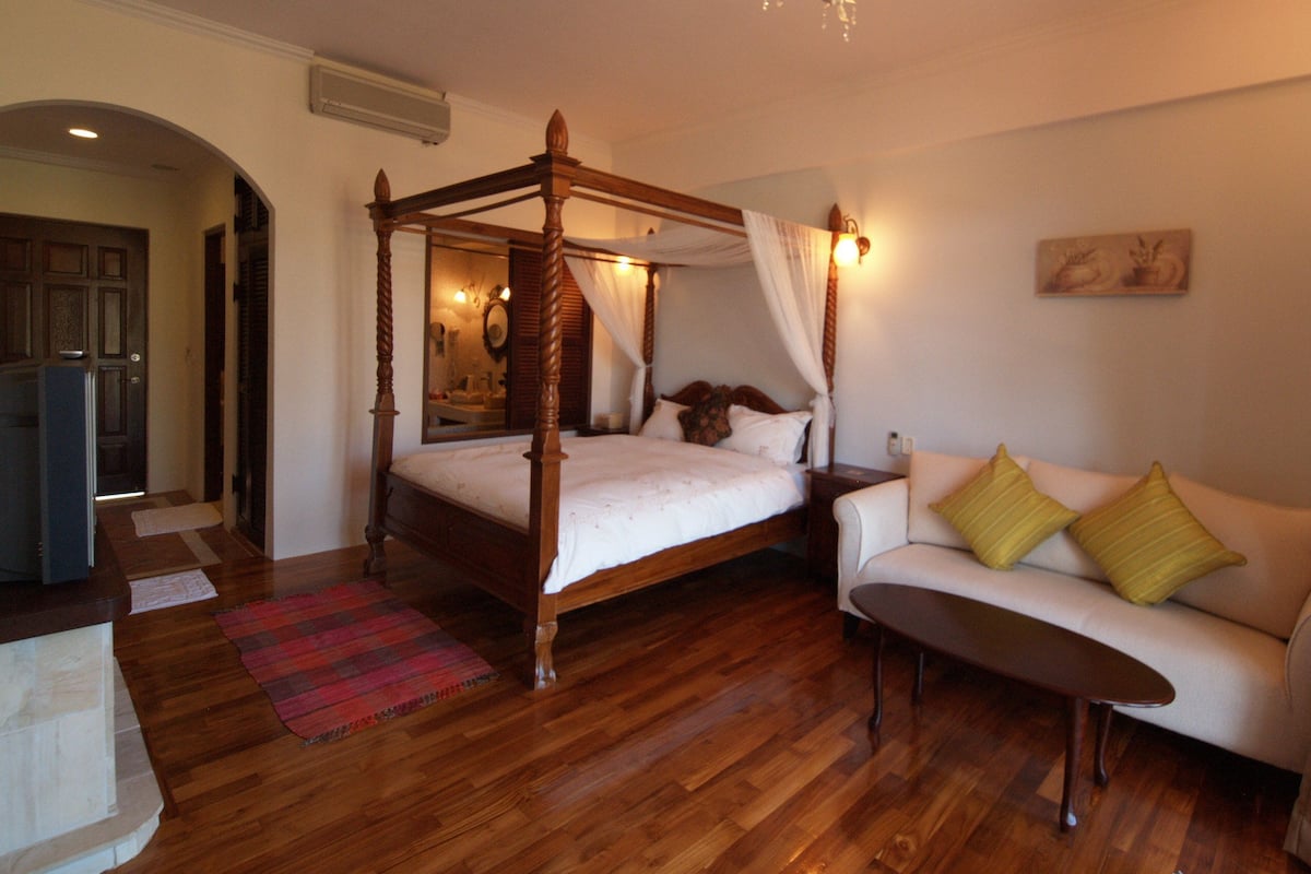 A four-poster bed with a canopy, a sofa with yellow cushions, and a wooden floor.