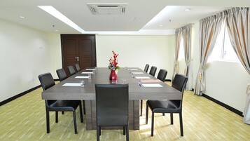 A conference room with a long table, chairs, a red vase with flowers, and a window with curtains.