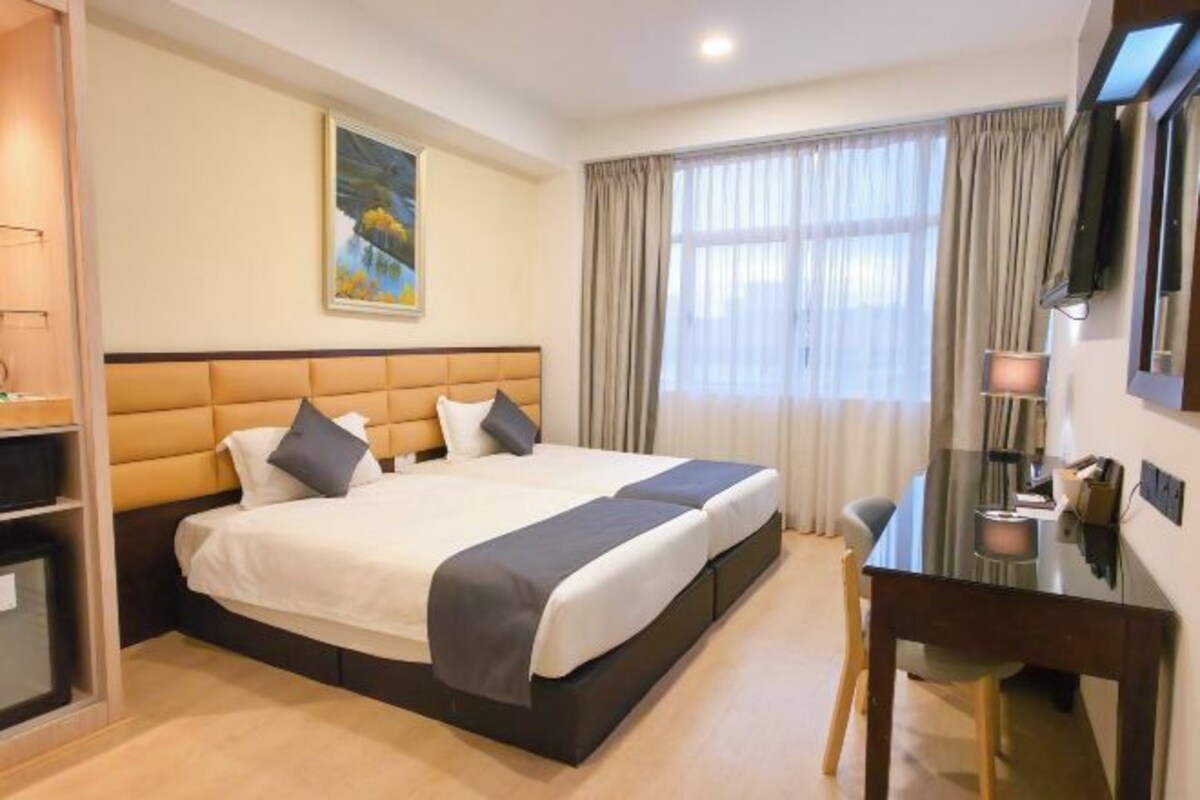 A hotel room with a large bed, a desk, a chair, a TV, and a painting on the wall.