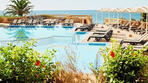 A pool area with lounge chairs and umbrellas, surrounded by greenery and a view of the sea.