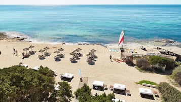 A beach with sun loungers, umbrellas, and a sailboat.