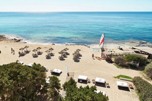 A beach with sun loungers, umbrellas, and a sailboat. - Hostal Es Pi 2 (Formentera)