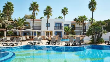 A swimming pool with lounge chairs, palm trees, and a white building with balconies.