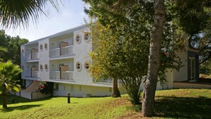 A multi-story building with balconies, surrounded by trees and grass.