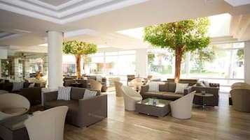 A spacious lobby with modern furniture, large windows, and indoor trees.