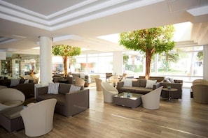 A spacious lobby with modern furniture, large windows, and indoor trees.