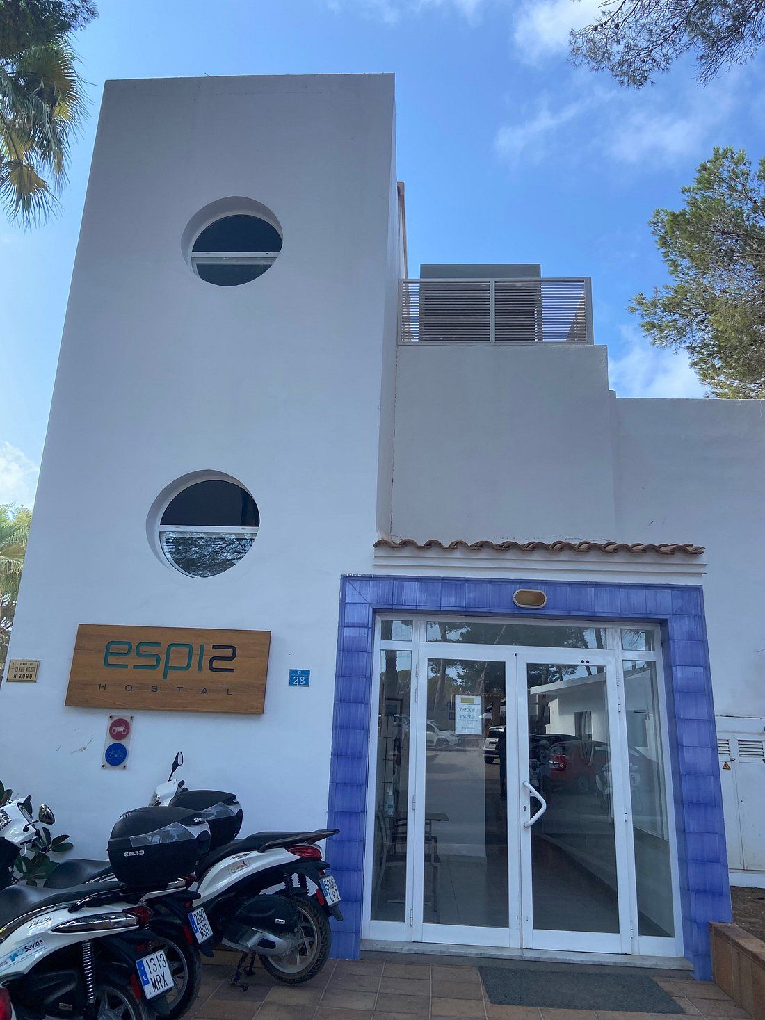 Un bâtiment sur lequel on peut lire l’inscription « esp12 HOSTAL » et où le chiffre « 28 » est peint sur le mur. La façade comporte deux fenêtres de forme circulaire.