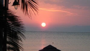 A sunset over a calm sea with a thatched umbrella and two people sitting under it. - Elena Hotel (Lokroi)