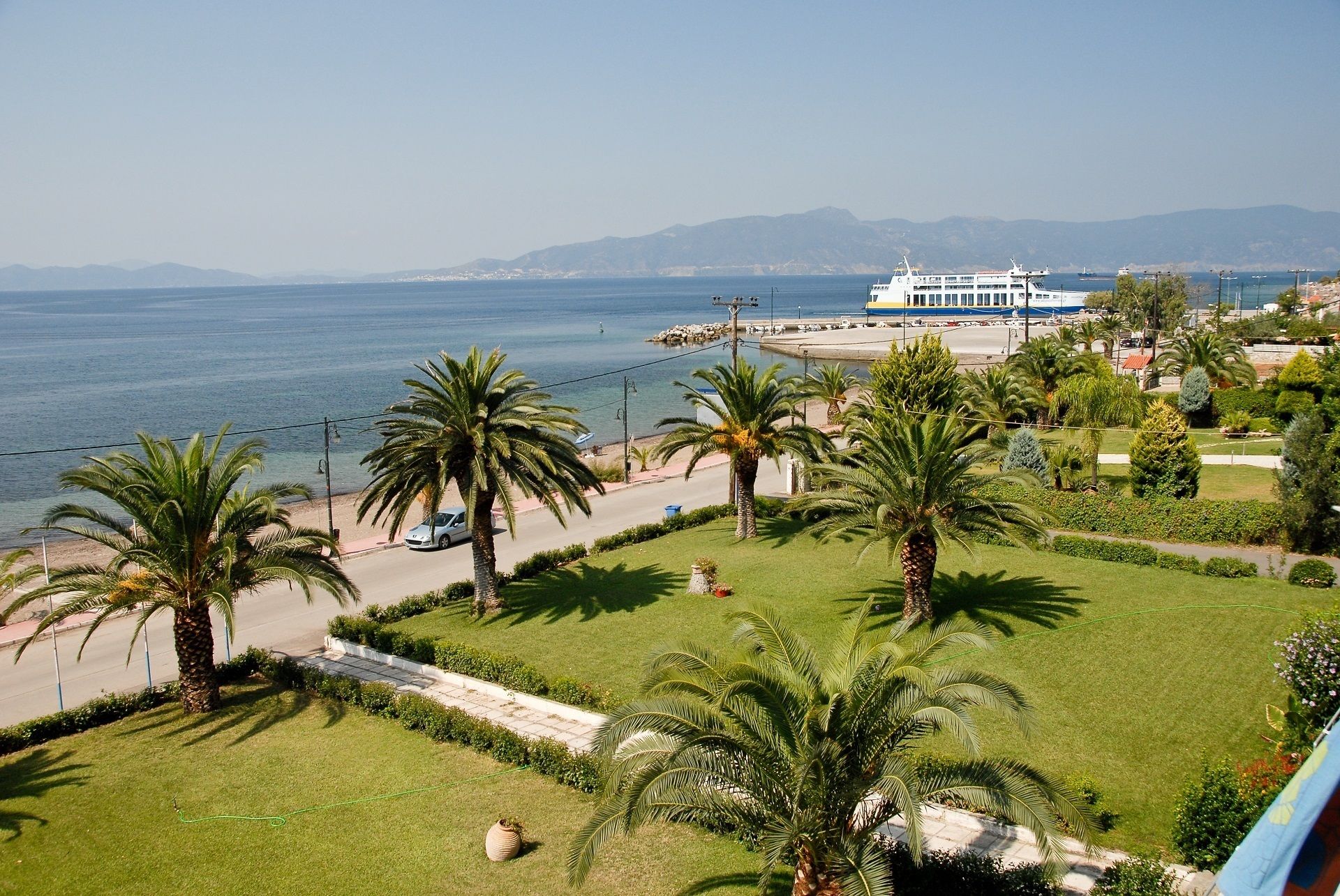 A coastal view with a large cruise ship docked at a port, palm trees, and a well-maintained grassy area.