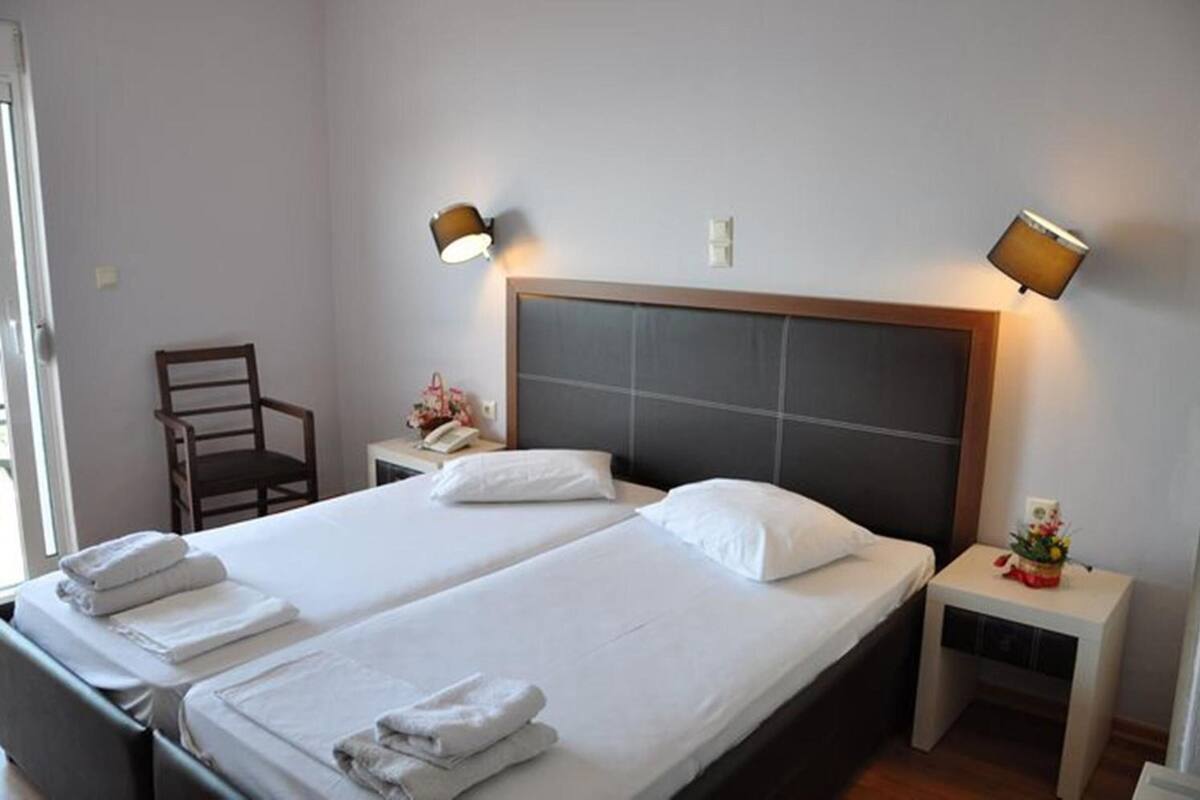 A hotel room with two beds, a chair, bedside tables, lamps, and a small table with a flower arrangement.