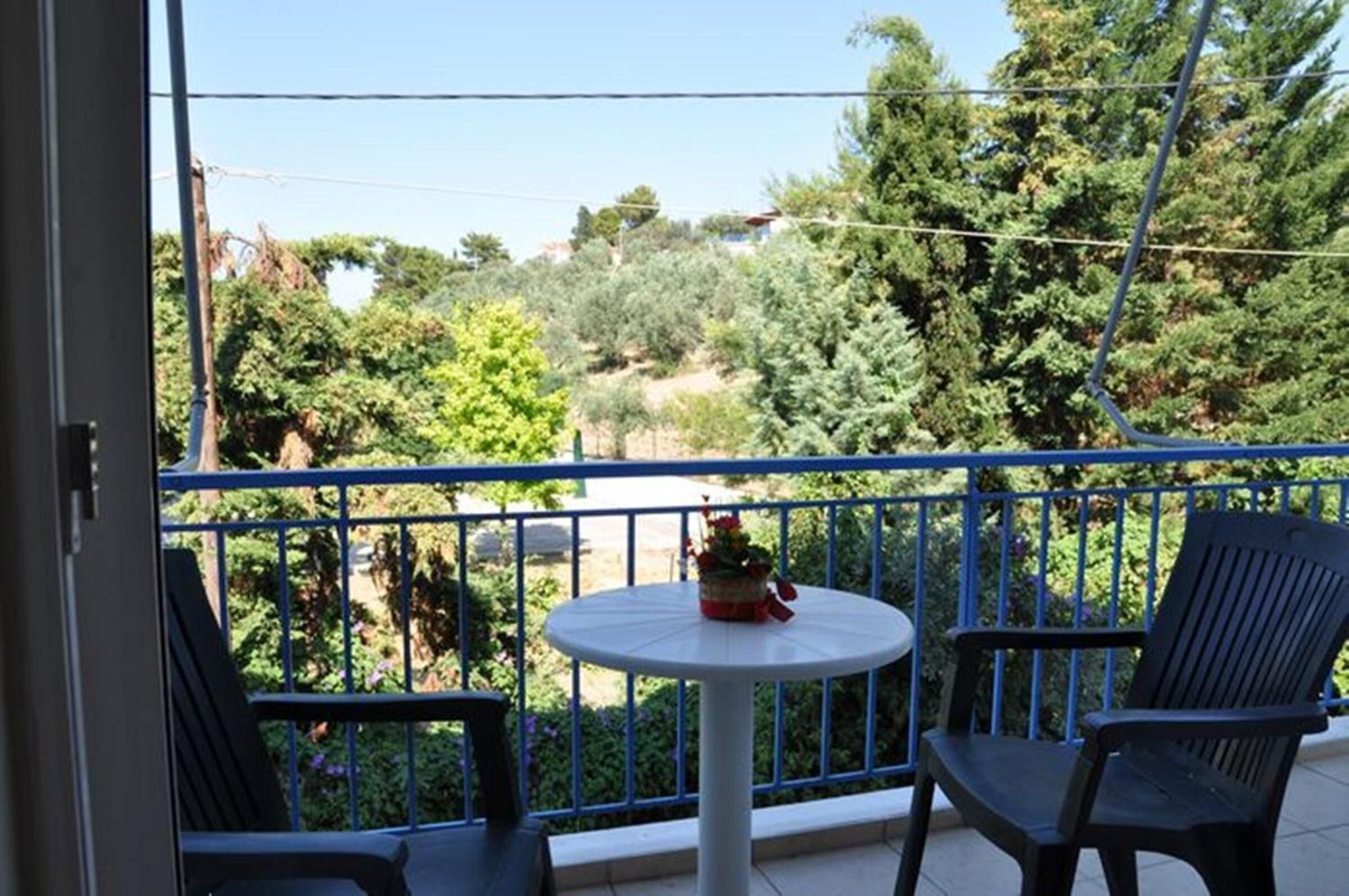 Ein Balkon mit zwei Stühlen und einem kleinen Tisch, mit Blick auf einen Garten mit verschiedenen Bäumen und Sträuchern.