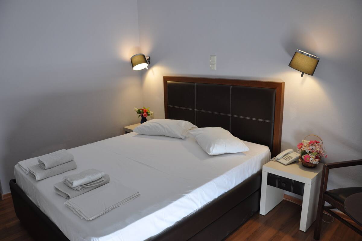 A neatly made bed with white linens and towels, a bedside table with a lamp, and a phone.