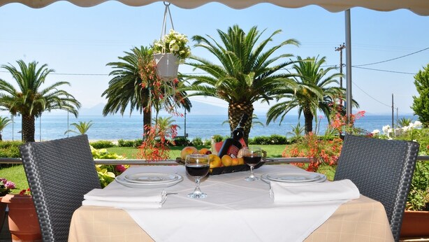 An outdoor dining area with a table set for two, overlooking a scenic ocean view. - Elena Hotel (Lokroi)