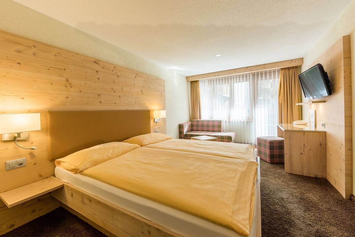 Habitación de hotel con dos camas, televisión, escritorio y ventana con cortinas.