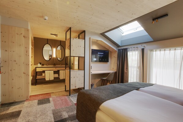 A hotel room with a large bed, a desk, a mirror, and a TV displaying 'DERBY'.